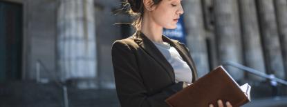Woman looking at a legal text in front of courthouse